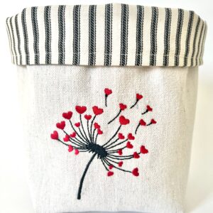 Off-white canvas basket embroidered with a black dandelion puff bursting with little hearts at the tips.