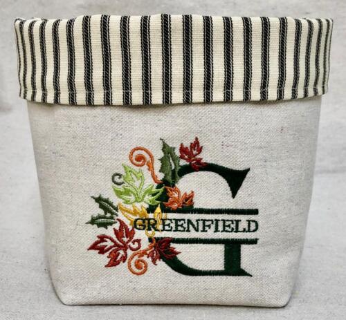 Natural canvas fabric bucket with black and white ticking cuff, emroidered with the initial G for Greenfield surrounded by a brach of autumn colored leaves